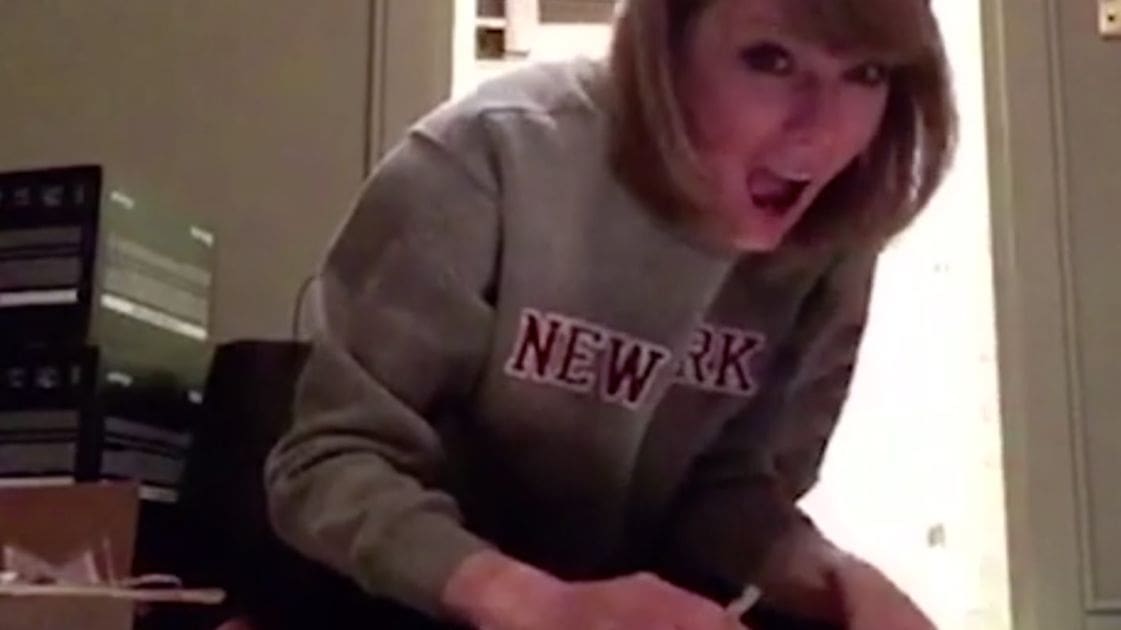 A young adult female wearing a gray, long-sleeved 'NEW YORK' sweatshirt in an indoor residential setting with natural lighting.