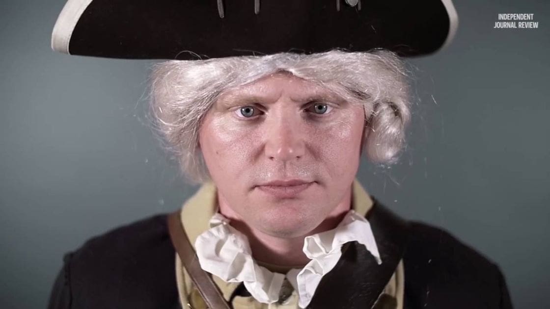 An adult male reenactor in 18th-century attire, including a tricorn hat and black coat with white cravat, stands against a plain dark gray background.
