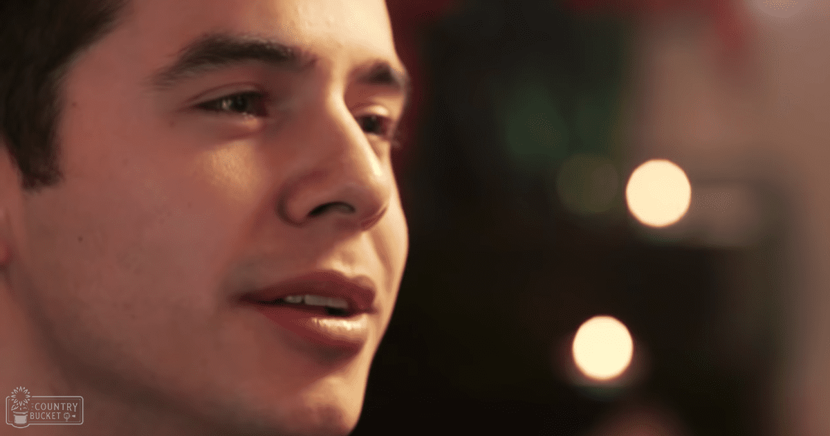 Young adult male face close-up indoors with warm string lights suggesting evening or holiday setting.