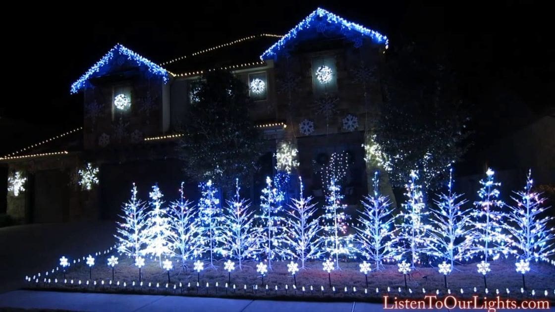A quaint house adorned with blue Christmas lights and snowflake decorations, set against a snowy winter backdrop.