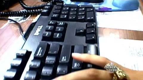An adult female wearing a gold ring interacts with a Dell-branded keyboard in an indoor workspace setting, illuminated by natural light.