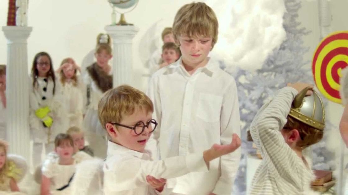 Children in a classroom setting with holiday decorations, white snowflake decorations on walls, natural light, daytime, indoor scene