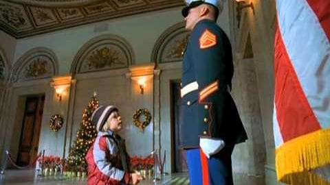 A young child in a red and blue winter jacket interacts with an adult in formal military attire at a ceremonial location, decorated for Christmas.