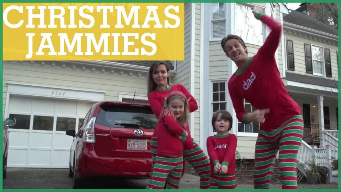A family of four dressed in Christmas jammies stands outside a suburban home with a red Toyota Prius parked nearby during late afternoon winter daylight.