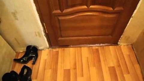 Two pairs of black high-heeled shoes on a polished hardwood floor near a wooden door with decorative paneling in an indoor residential space, suggesting preparation for departure or arrival.
