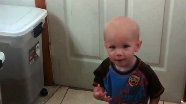 Toddler wearing a loose-fitting, short-sleeved blue t-shirt with a red and white police graphic design indoors in a residential setting.
