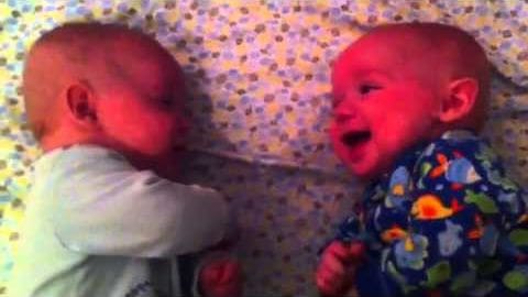 Two infants in a hospital setting with light green and white floral onesie and dark blue colorful floral onesie on a patterned bedspread with soft muted colors.