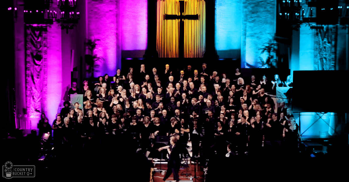 A choir performing on a colorful stage with a cross backdrop in an indoor church setting during evening light.
