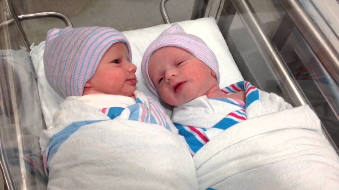 Two infants wrapped in striped blankets in a clinical hospital setting with soft lighting.