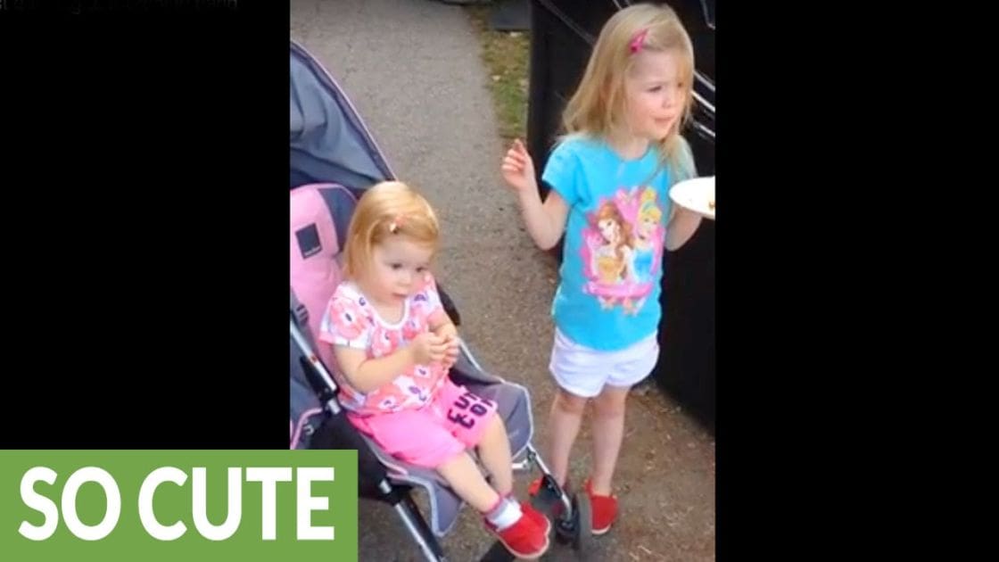 Two young children in an outdoor setting with a pink stroller, wearing colorful clothing and holding a small plate or dish.