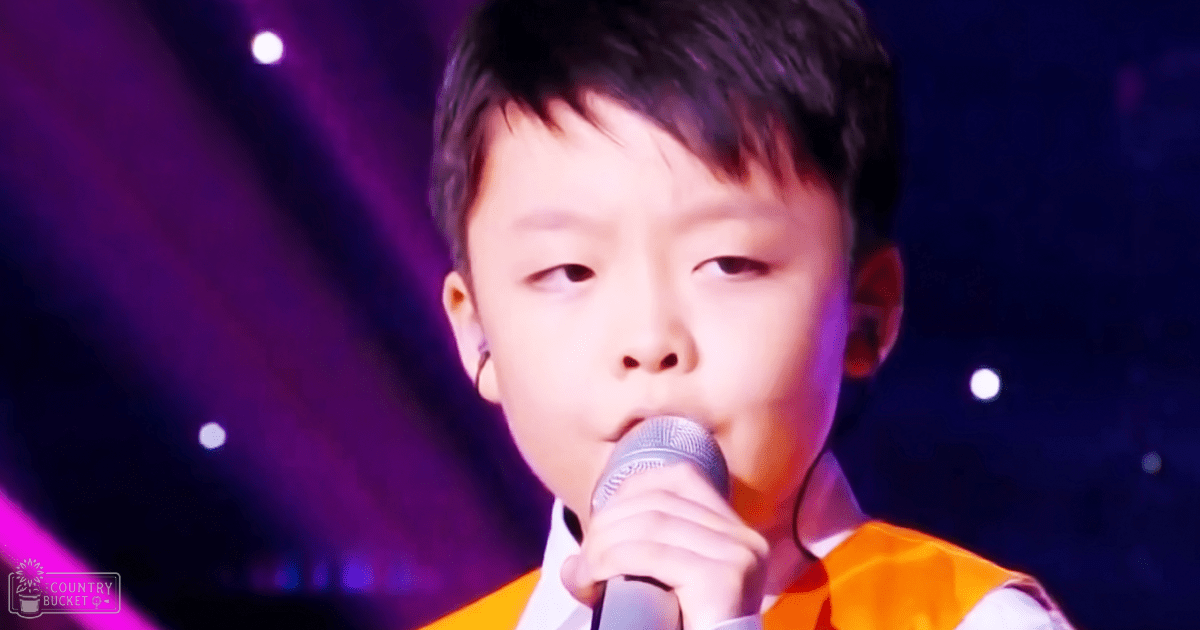 A child in a formal shirt and orange vest performs on stage with purple lighting.