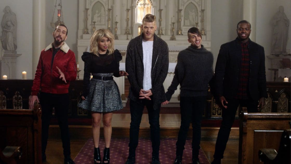 A group of five young adult individuals in a well-lit indoor church setting with ornate wooden pews, statues, candles, and stained glass windows.