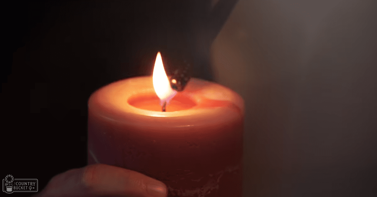 A single lit red candle with a bright wick burning in an indoor setting, surrounded by darkened surroundings.