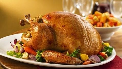 A roasted turkey garnished with vegetables on a white plate, set in an indoor dining area with warm golden lighting.