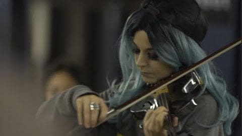 A young adult female playing a violin indoors in an architectural setting during neutral daylight.