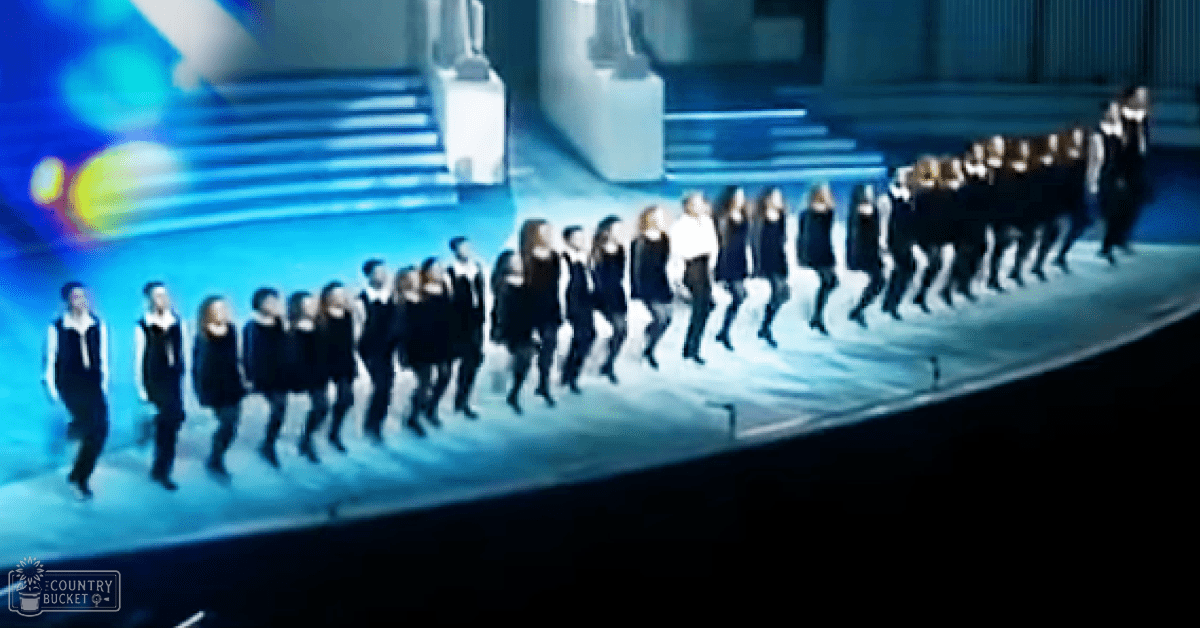 Young adults performing in a coordinated outfit on an indoor stage with blue and white lighting, suggesting a concert or event setting.