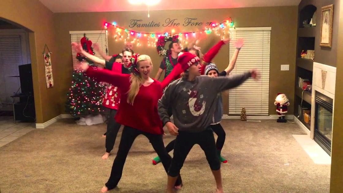 Young adults dancing in a living room decorated for Christmas with festive lights and Santa Claus decorations.