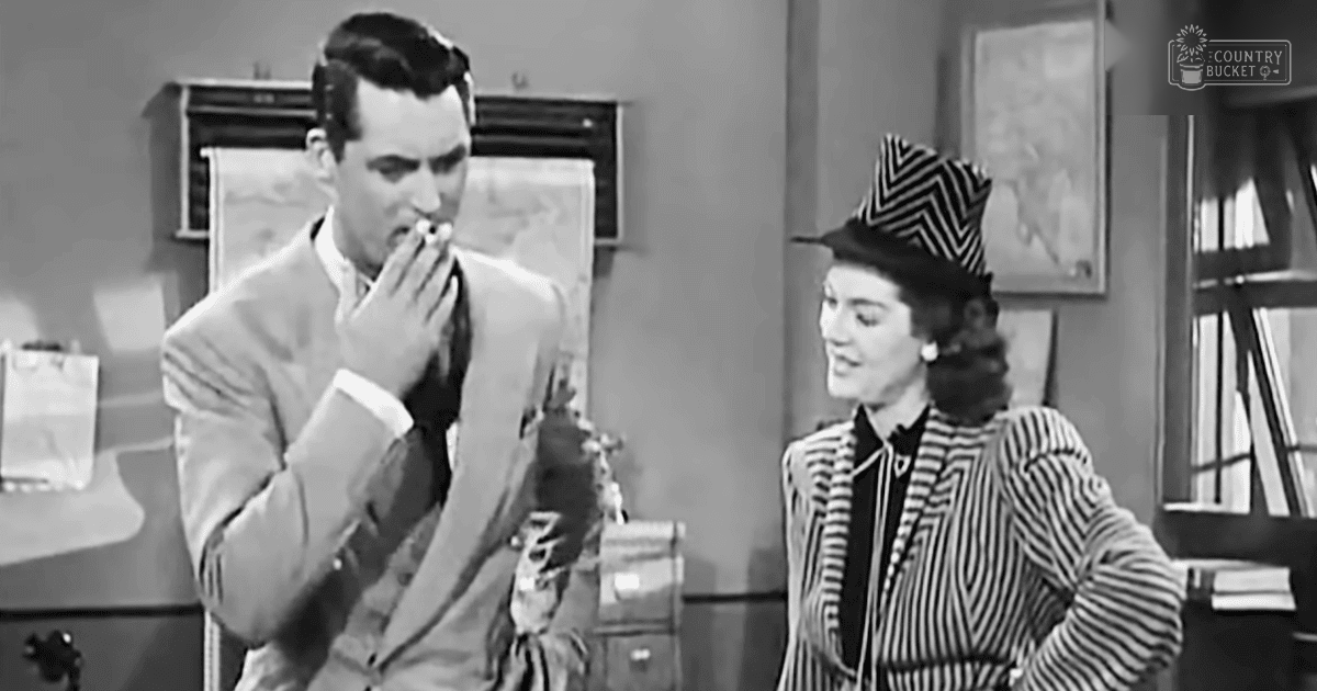 A man in a mid-20th century light-colored suit and white shirt with a dark tie smokes a cigarette in an office setting; nearby is a woman wearing a black-and-white striped jacket, high collar hat, and earrings.