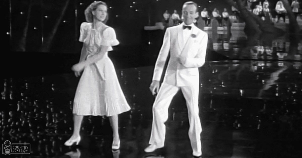 A classic dance scene from a Hollywood film set during the 1940s, with two formally dressed performers on an indoor stage with reflective surfaces and dark backdrop.