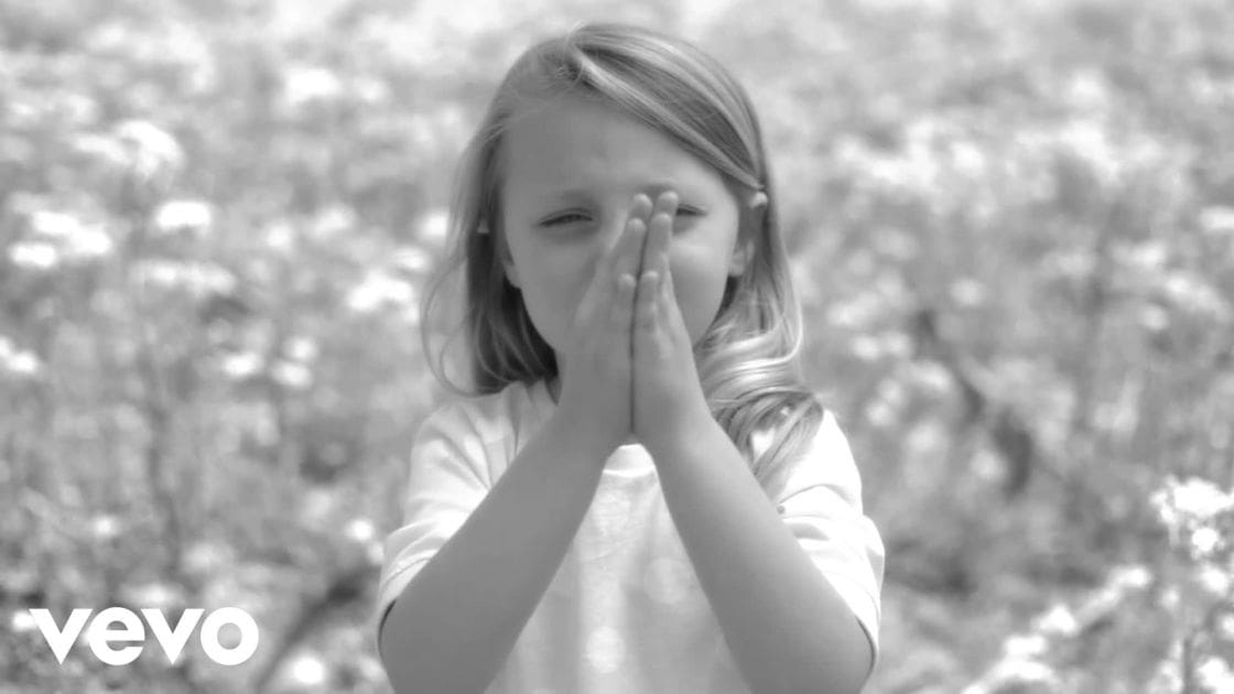 A child wearing a white long-sleeved shirt outdoors with trees in the background.
