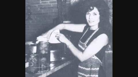 A young adult female wearing a sleeveless dress with horizontal stripes in an indoor kitchen setting, engaging in food preservation activities.