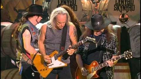Lynyrd Skynyrd concert scene with adult male musicians in casual attire performing under stage lighting.