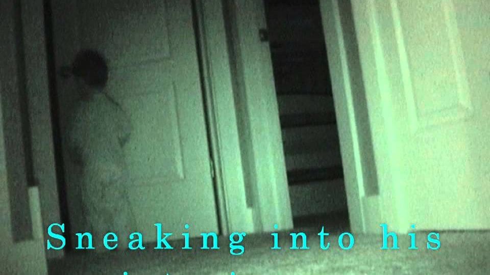 A small dark-furred animal near a wooden door indoors, with dim evening light casting shadows on neutral walls.