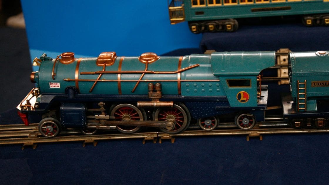 A detailed model steam locomotive with passenger cars, labeled 'LIONEL', displayed indoors against a blue backdrop.