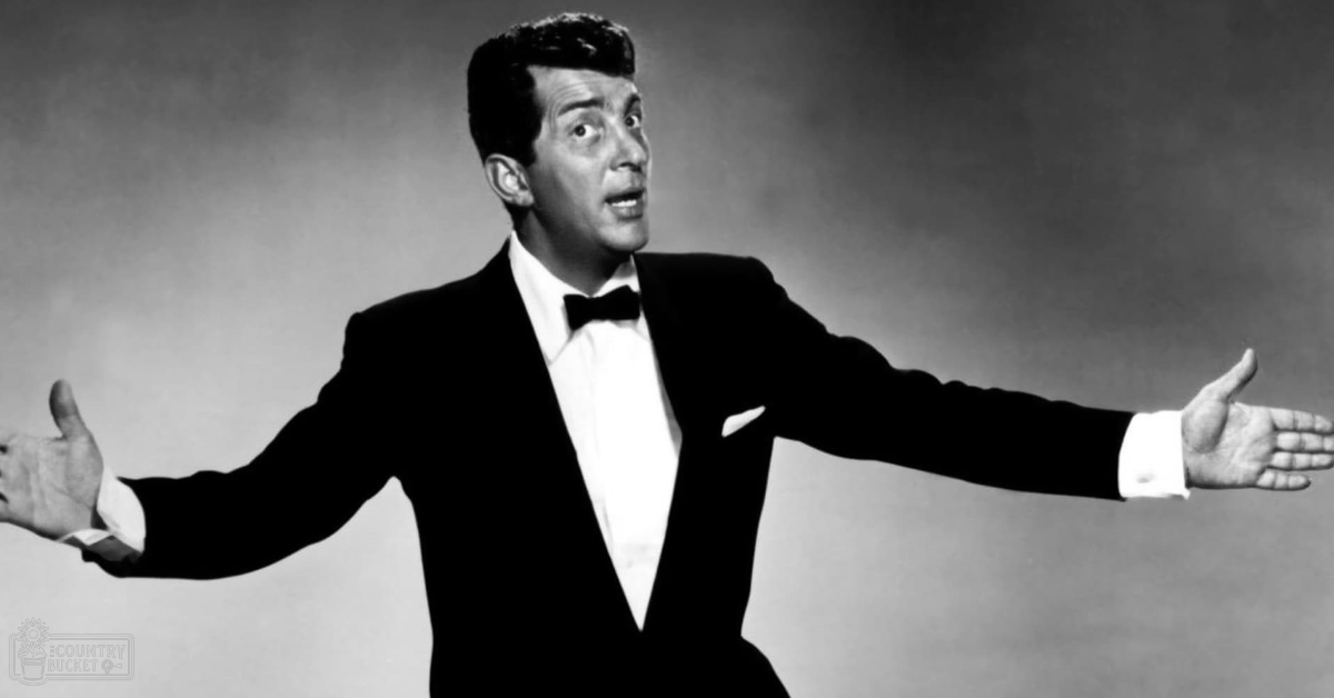 An adult male singer in a well-fitted black tuxedo with white shirt and bow tie, standing indoors under professional lighting.