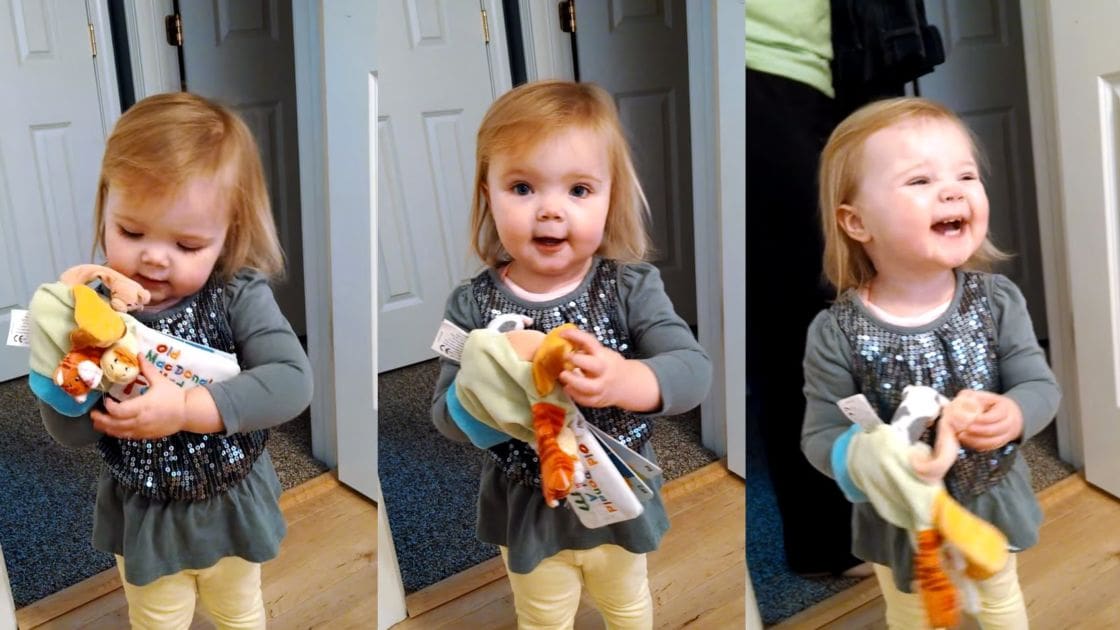 A toddler in an indoor setting, wearing a dark green long-sleeved shirt with sequins and light yellow pants. The background includes white doors and a dark blue carpeted area.