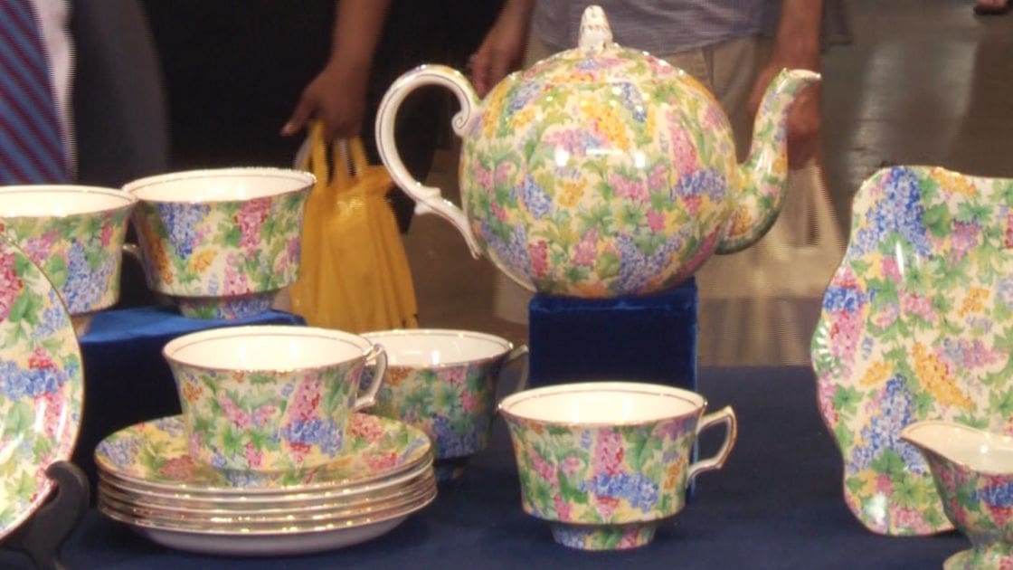 An indoor event with a vibrant floral tea set displayed against a backdrop of people wearing casual attire.