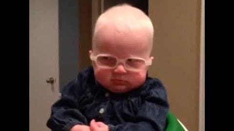 An infant male in a dark blue button-up shirt indoors, wearing clear-framed glasses.