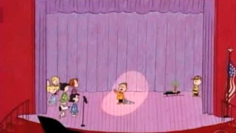 Children performing on a stage with red walls and purple curtain backdrop, spotlight illuminating the center area.