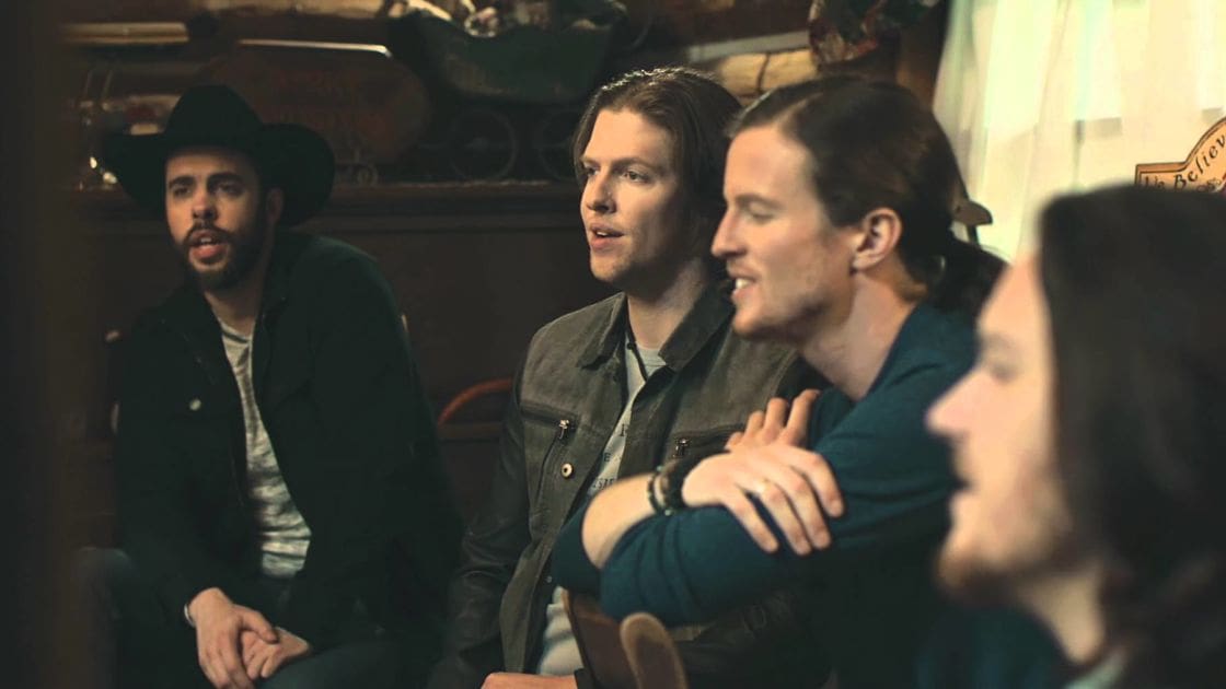 A group of young adults in a cozy bar setting with wooden shelves, various bar-related items, and a 'We Believe' sign on display.