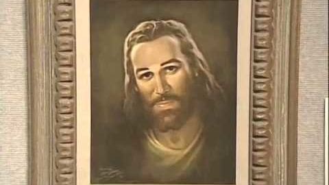 An ornate-framed portrait of Jesus Christ indoors, rendered with muted earth tones and historical style; light source above subject casting subtle shadows on face.