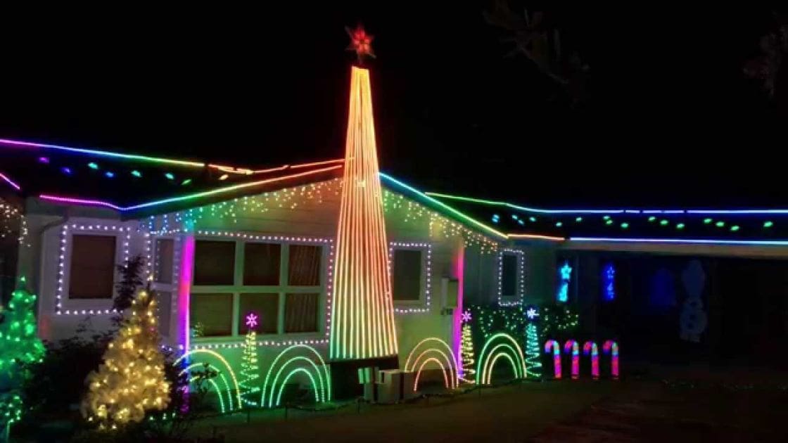 A house adorned with colorful Christmas lights in a residential neighborhood at night.