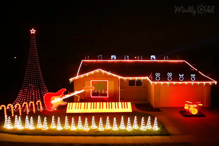 A residential neighborhood decorated for Christmas with a large tree, red electric guitar, drums, spiral lights at night.