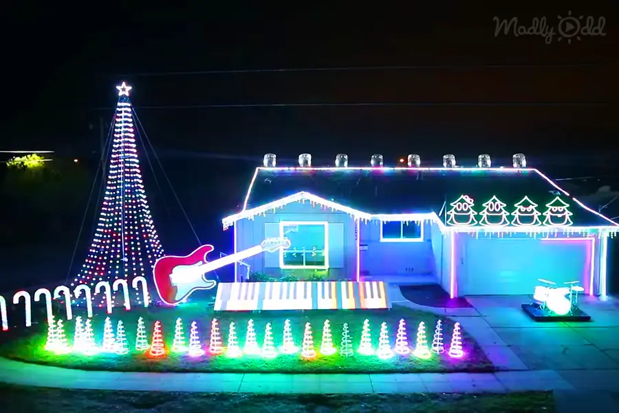 An outdoor residential area decorated for Christmas with a large tree, neon lights, and cone-shaped decorations at night during winter.