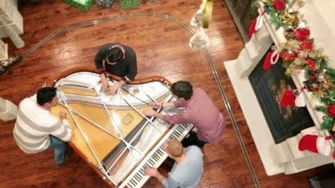 A group of individuals playing a grand piano in a Christmas-decorated living room.
