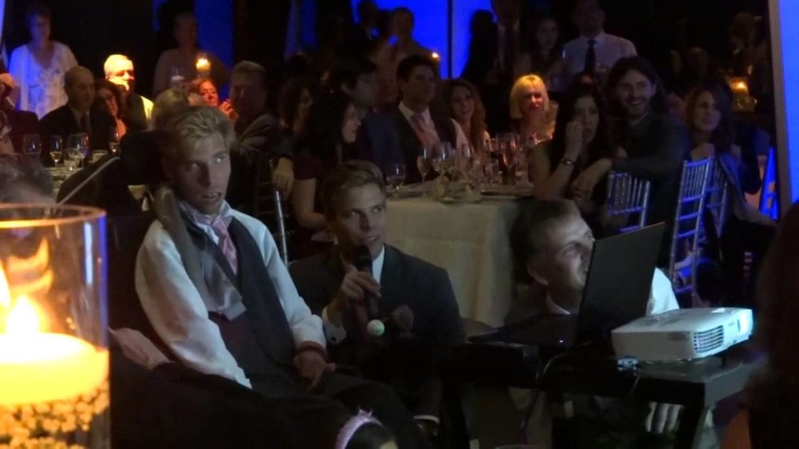 A young adult male in a formal setting, possibly an event or banquet hall.