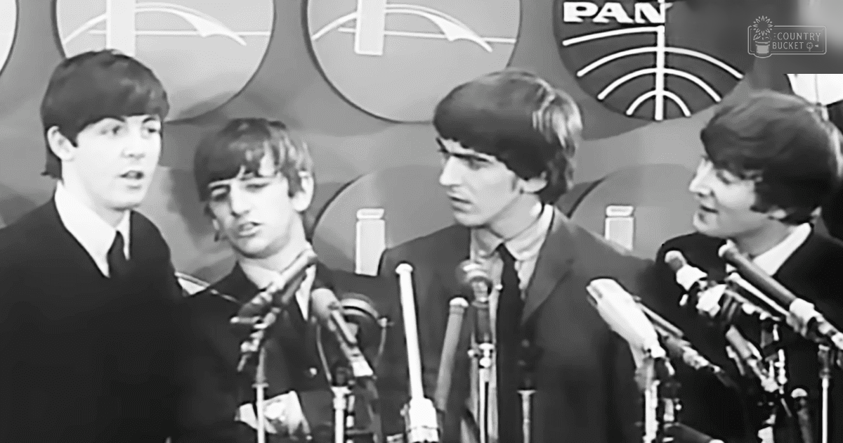 Four young adult males in dark suits, microphones and 'Pan Am' logos behind them at an indoor event or press conference.