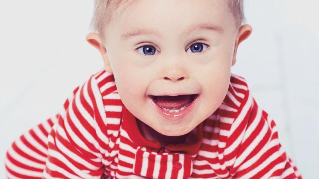 A baby wearing a snug-fitting, long-sleeved, red-and-white striped shirt with a round neckline, set against a plain white indoor backdrop.