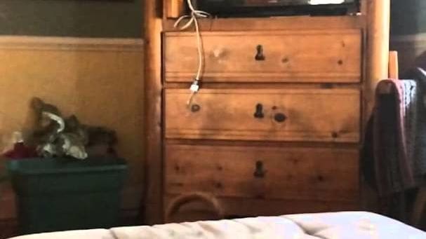 An older adult male figure stands in a bedroom scene with personal belongings scattered around, suggesting a lived-in space.