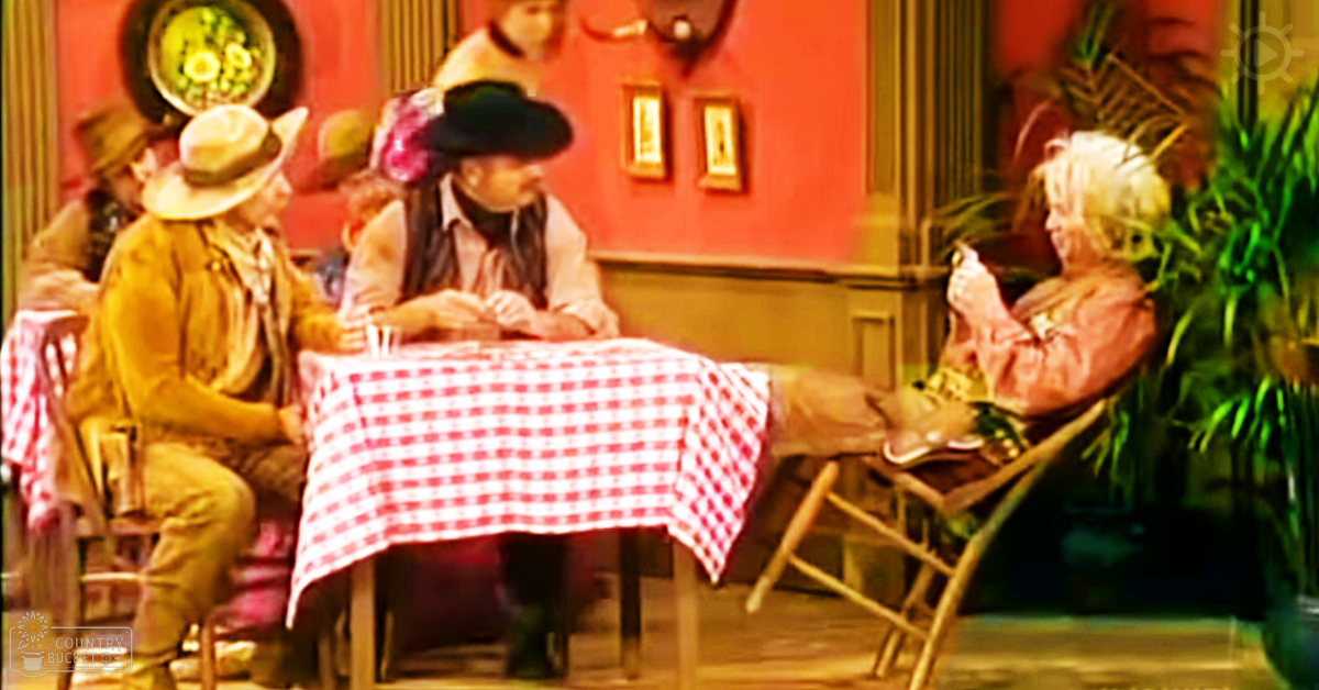 A group of adults in a cozy indoor restaurant setting, wearing wide-brimmed hats with floral details and light-colored attire under warm artificial lighting.