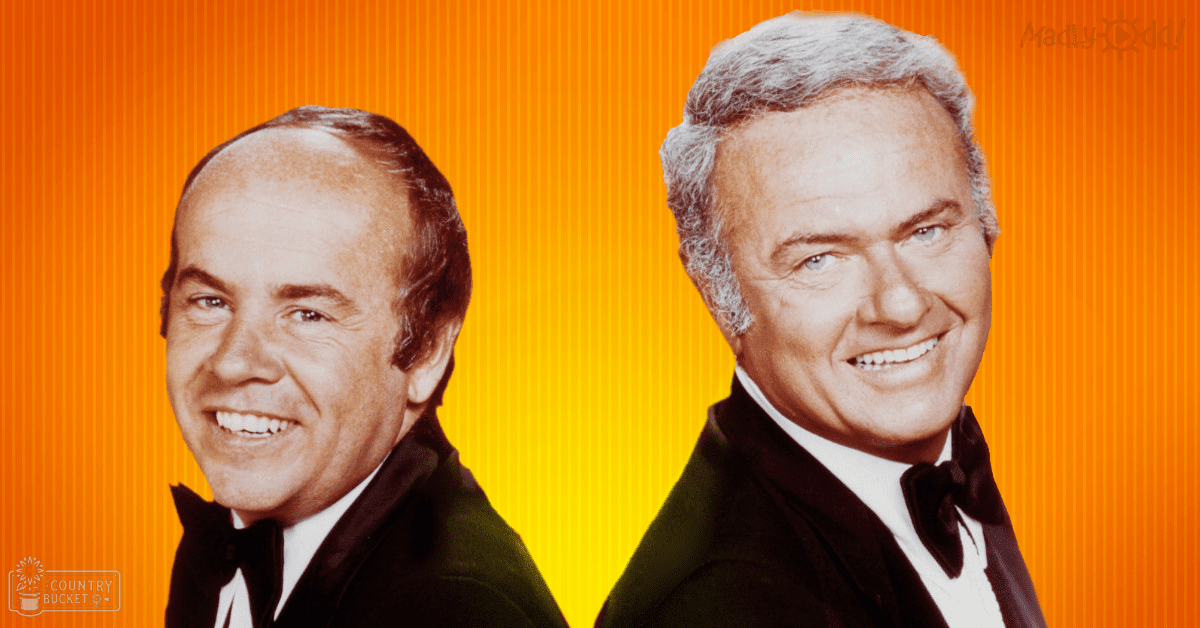 Two middle-aged men dressed in dark suits with white shirts and black bow ties, posed against a solid orange backdrop.