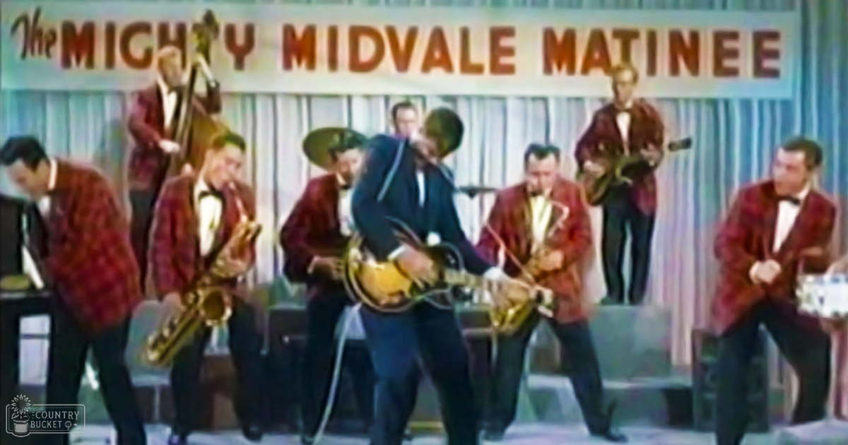 A musical performance at 'The Mighty Midvale Matinee' on an indoor stage with performers wearing red plaid blazers, white shirts, black bow ties, dark trousers, and dark shoes. They are playing various instruments like saxophones and trombones.