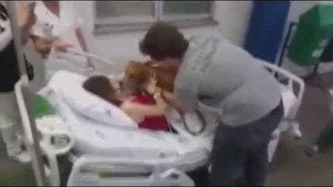 A toddler in a hospital bed alongside an adult female healthcare professional wearing a stethoscope; scene inside a medical facility with artificial lighting typical of clinical environments.