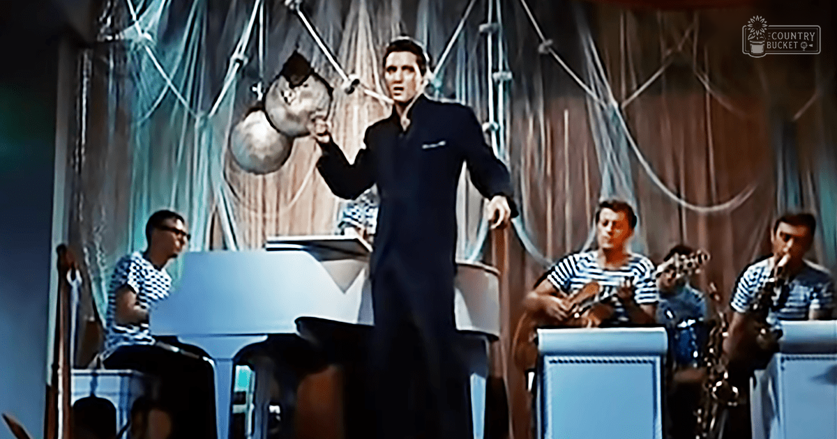 Indoor performance scene with adult male performers in formal attire, musical instruments, and dramatic background artwork.