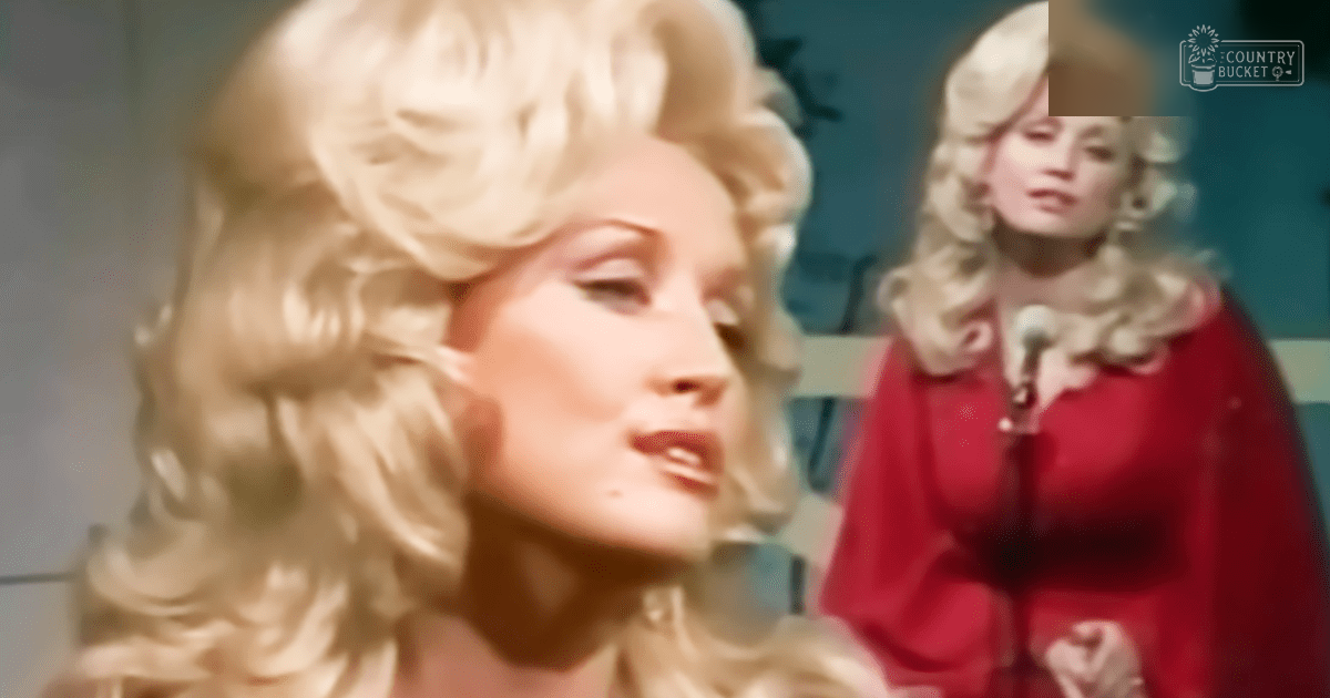 Two adult females with long, curly blonde hair stand indoors; one wears a red vintage-style garment with high neckline and wide sleeves. The setting suggests a performance venue like a theater or concert hall.