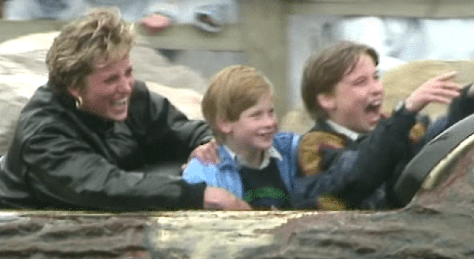 Adult female with short blonde hair, wearing a dark green jacket and gold hoop earrings, accompanied by two children in blue shirts at an indoor theme park during winter.